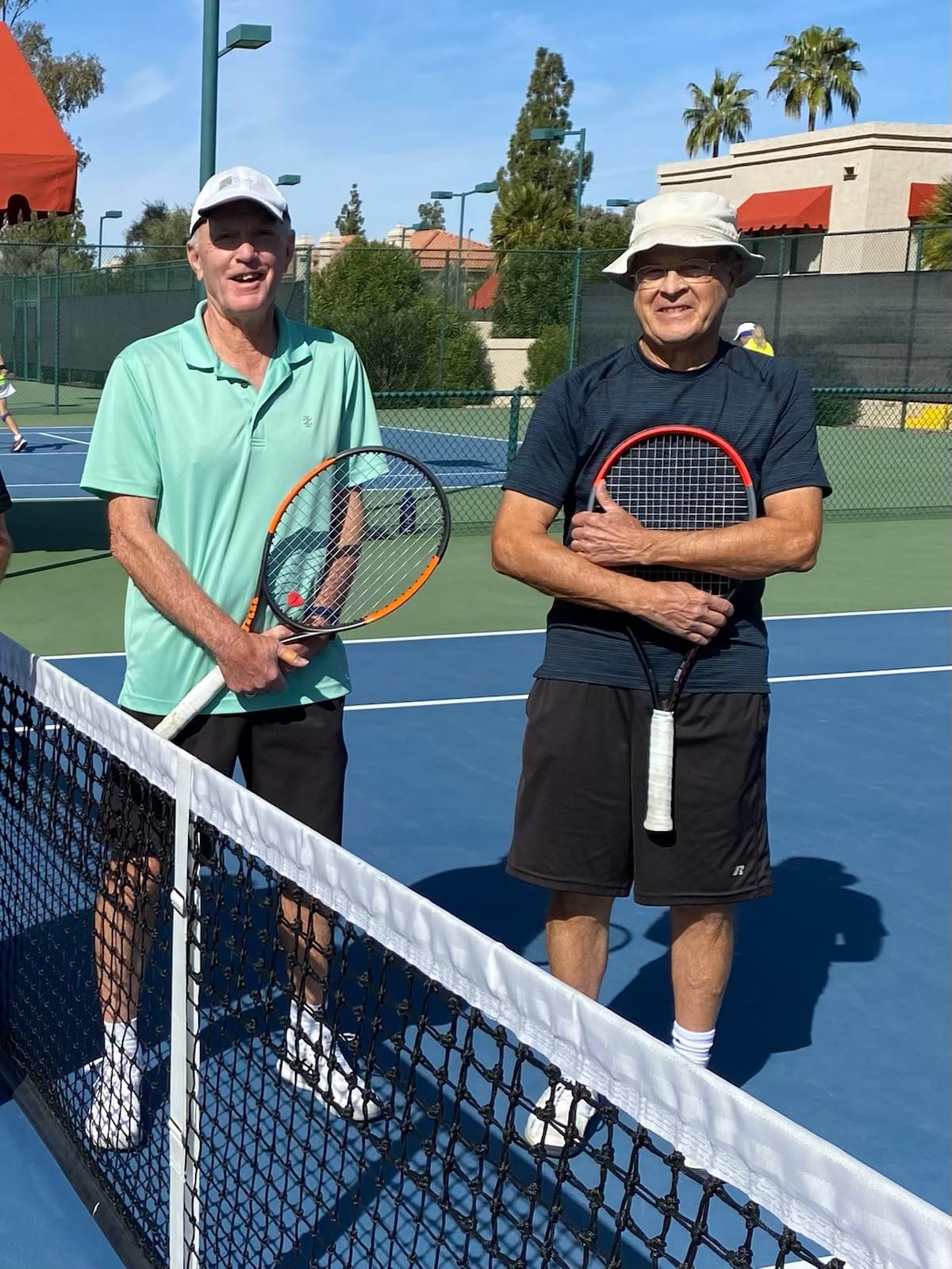 Two over-60 champions holding racquets beside the net.