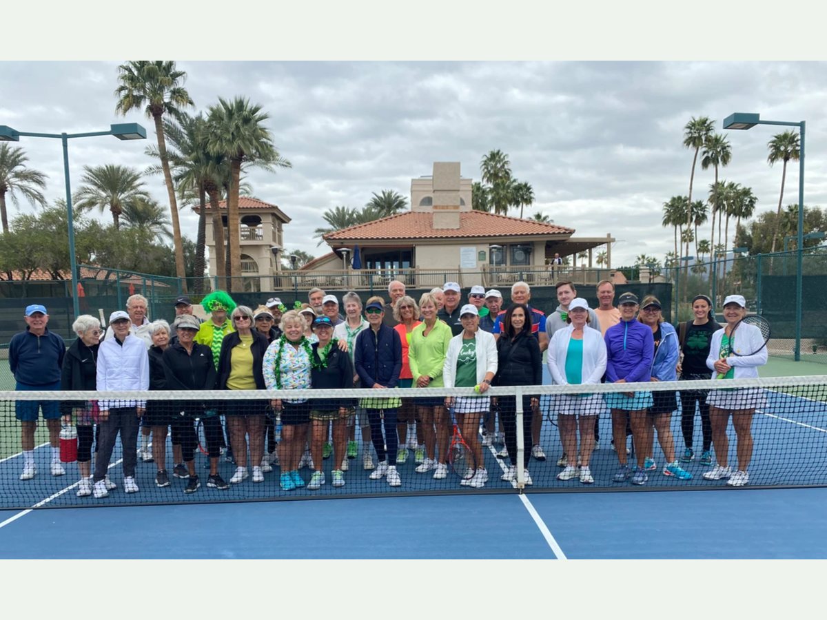 St. Paddy's Day Tennis Mixer participants gathered behind the net on a cloudy day.