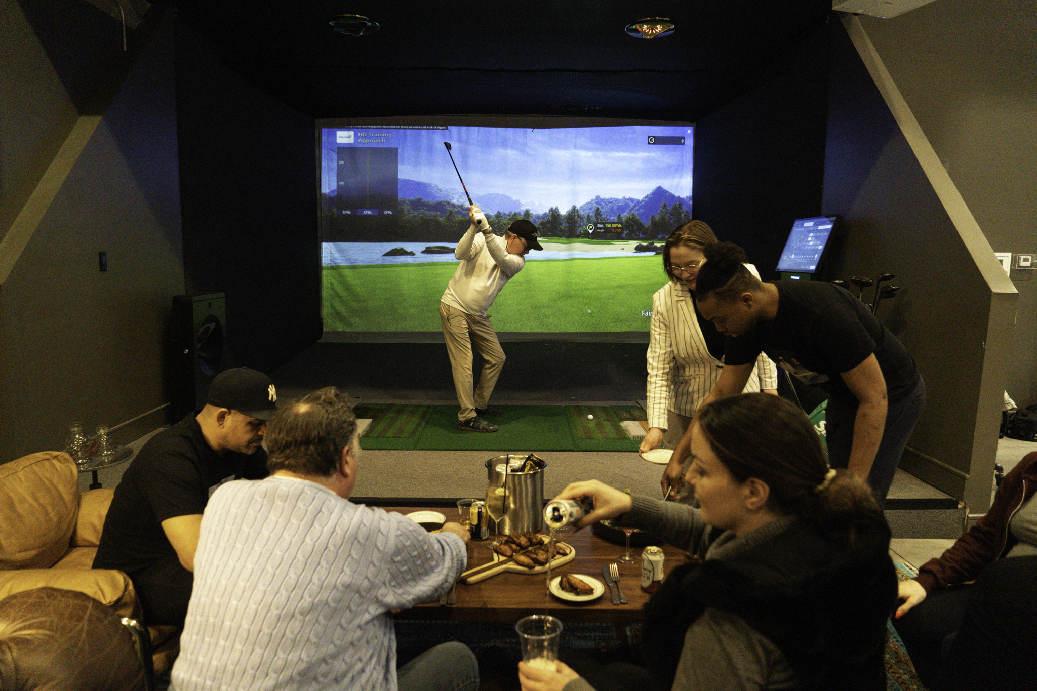 Friends dining and drinking beside a Ballers golf simulator