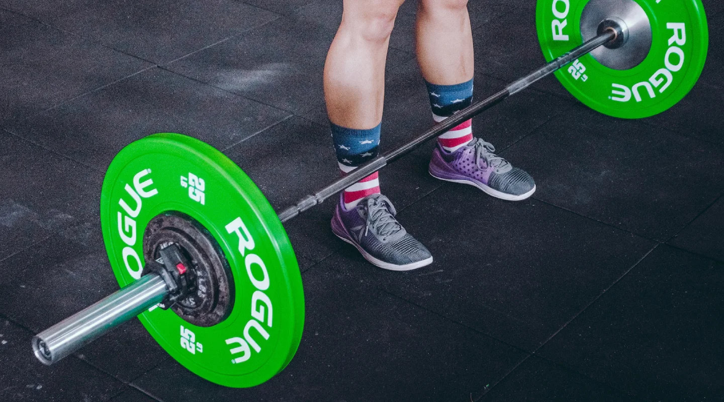 Athlete preparing to lift a barbell with green bumper plates at The Strength Yard in West Palm Beach, FL.