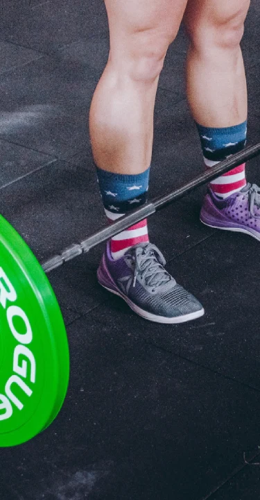 Athlete preparing to lift a barbell with green bumper plates at The Strength Yard in West Palm Beach, FL.