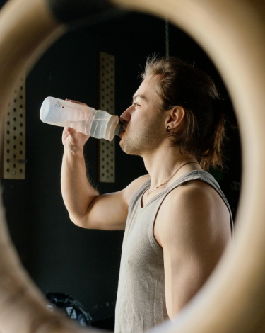 Athlete drinking water between workouts near gymnastic rings at The Strength Yard in West Palm Beach, FL.