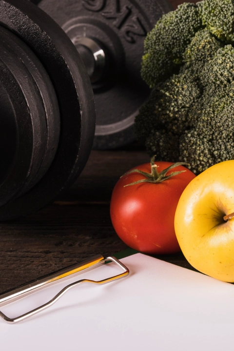 Dumbbell and fresh vegetables representing nutrition and strength training at The Strength Yard in West Palm Beach, FL.
