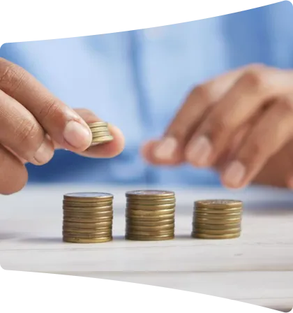 Close-up of a person stacking coins into three piles of increasing height on a wooden surface, symbolizing saving or financial growth.