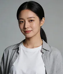 Portrait of a young Asian woman with long black hair tied back, wearing a white t-shirt and a gray open shirt, smiling gently against a plain gray background.