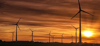 Wind turbines on a horizon silhouetted against an orange sky at sunset.