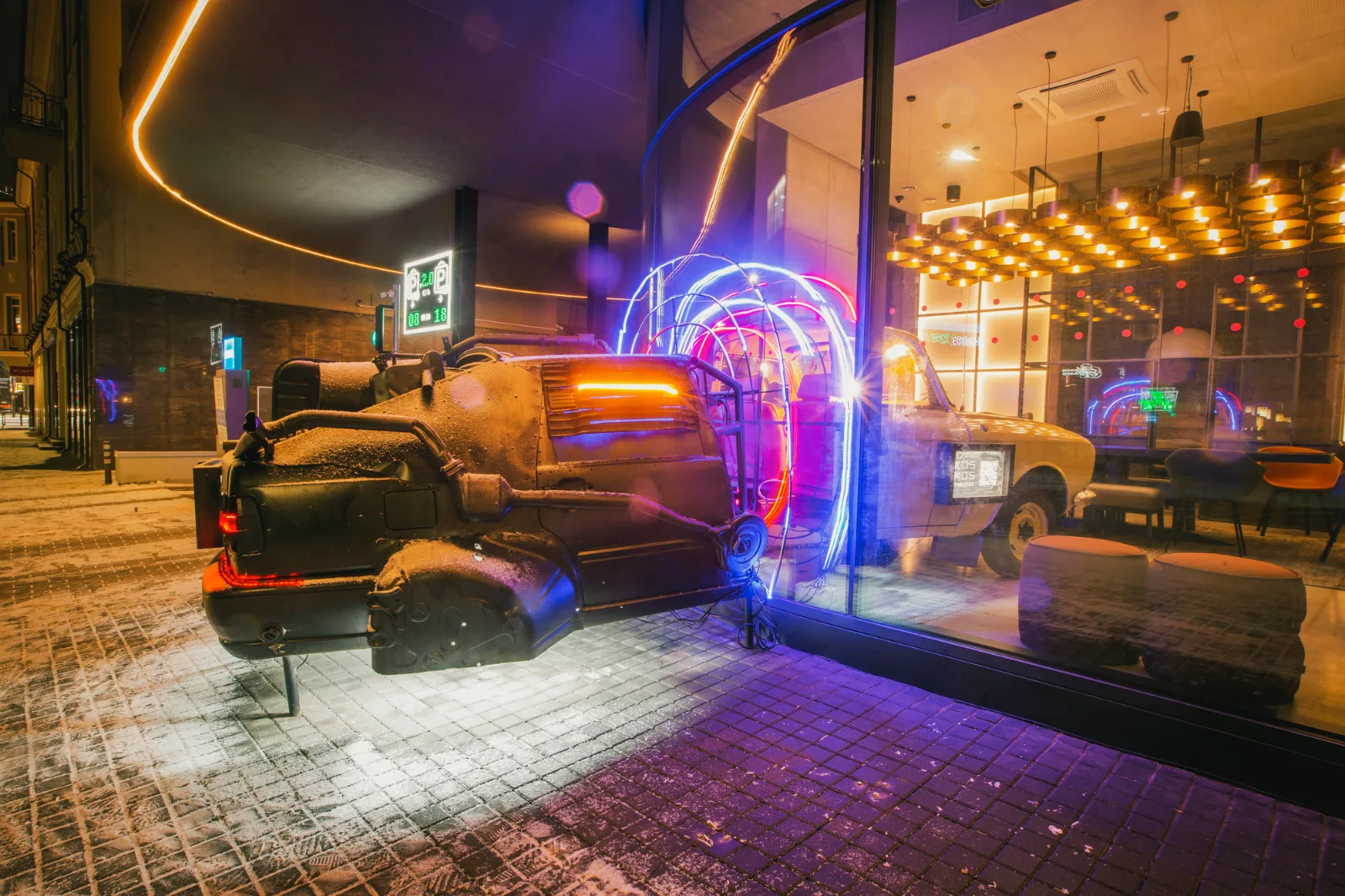 Kosmos Car – a car with neon tubes beside a lit café window at night