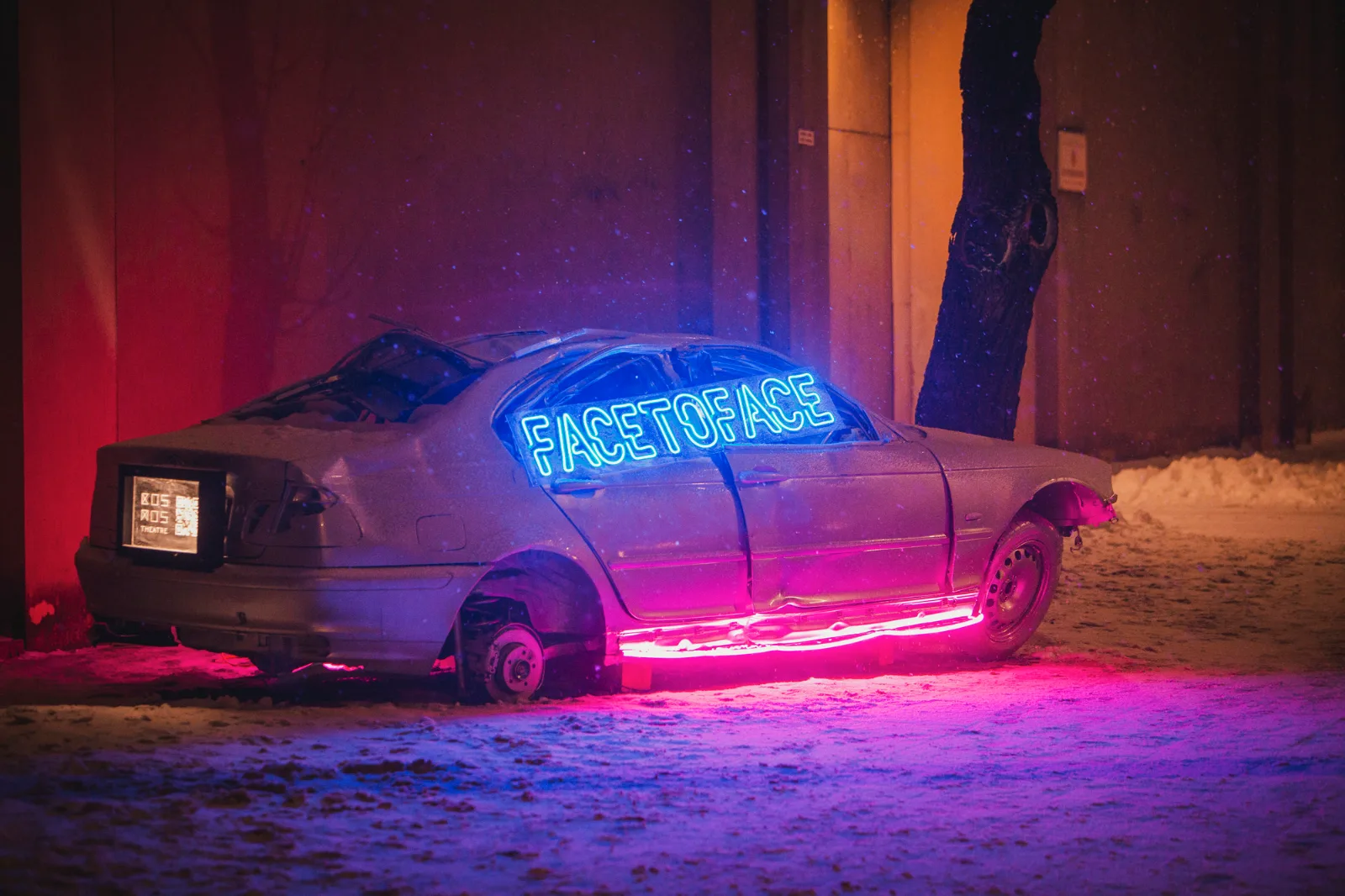 Kosmos Car – a snow-covered car with glowing lettering beside a red wall