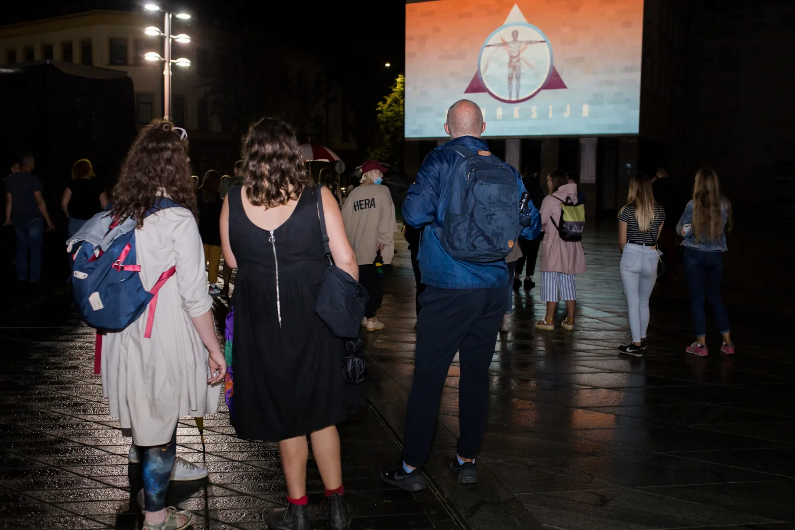 #Protest – spectators walk across a square at night towards a projection