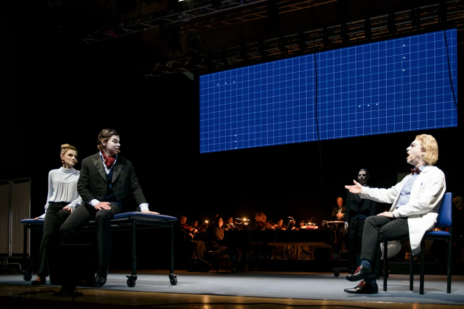 The Man Who Mistook His Wife For a Hat – singers on stage beneath a projected grid of dots, the orchestra behind