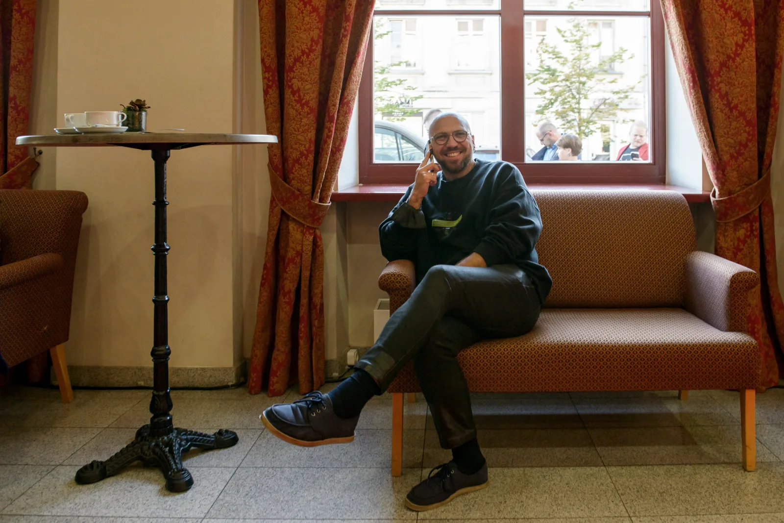 The Man Who Mistook His Wife For a Hat – a man sits on a sofa by a window in a theatre foyer