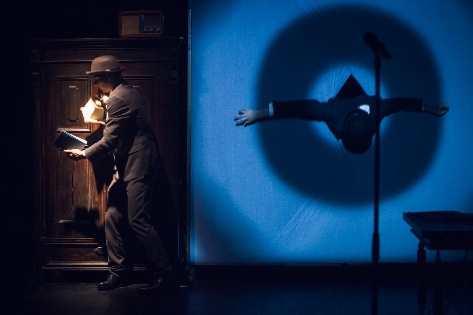 Kafka Insomnia – an actor in a hat by a door, a figure in a circle of light on the wall