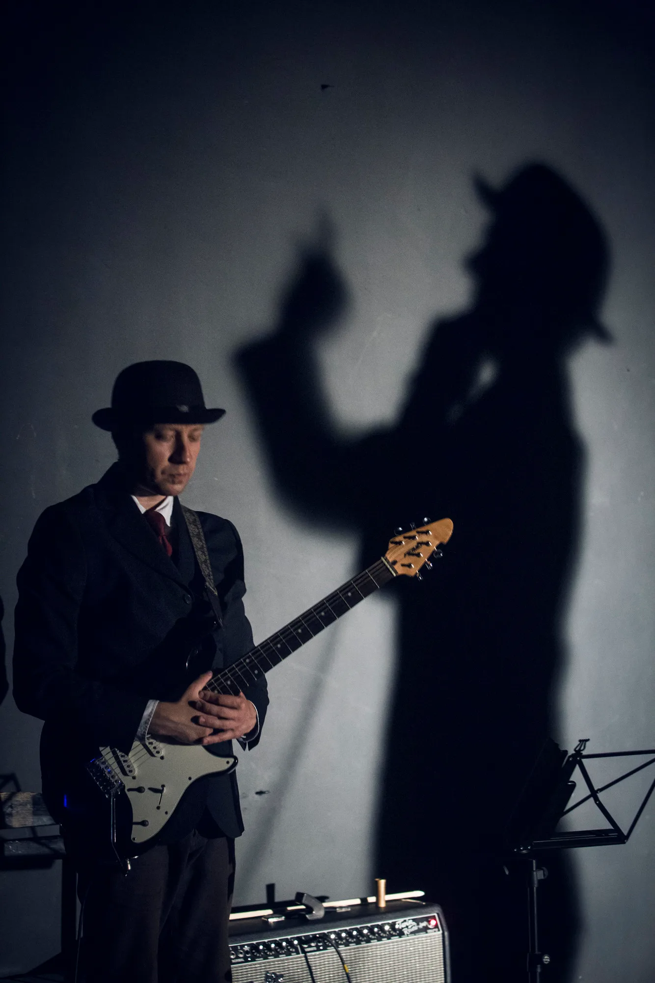 Kafka Insomnia – a guitarist in a bowler hat plays beside his large shadow on the wall