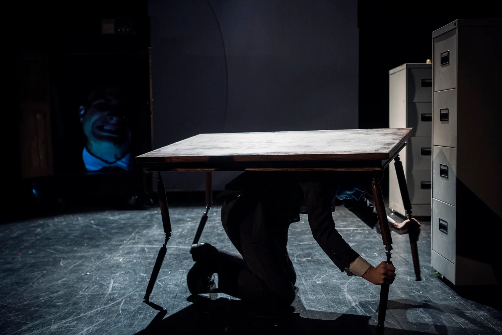 Kafka Insomnia – an actor crawls under a table, a face projected on a wardrobe behind him