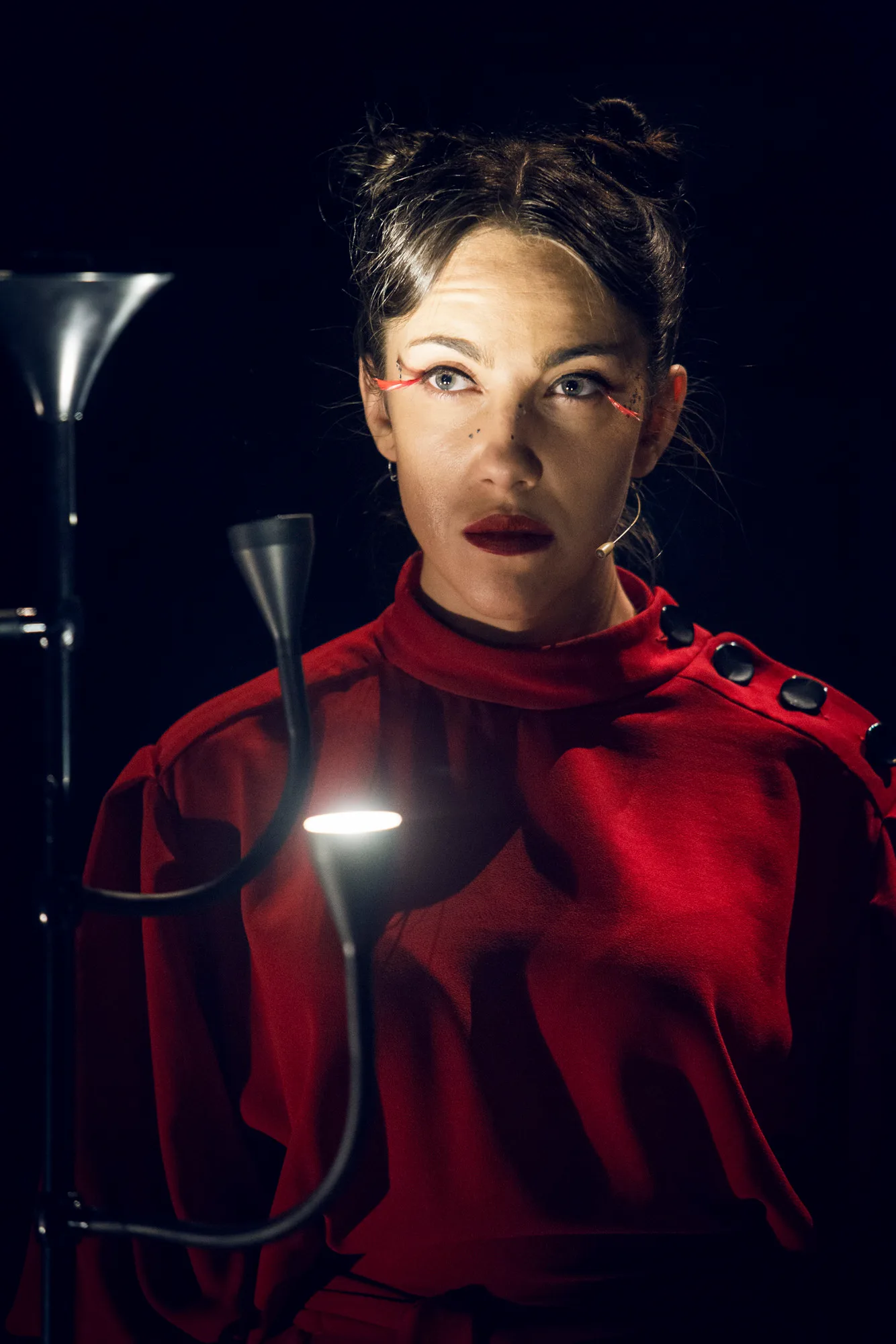 Kafka Insomnia – a woman in red lit by a small lamp looks into the camera
