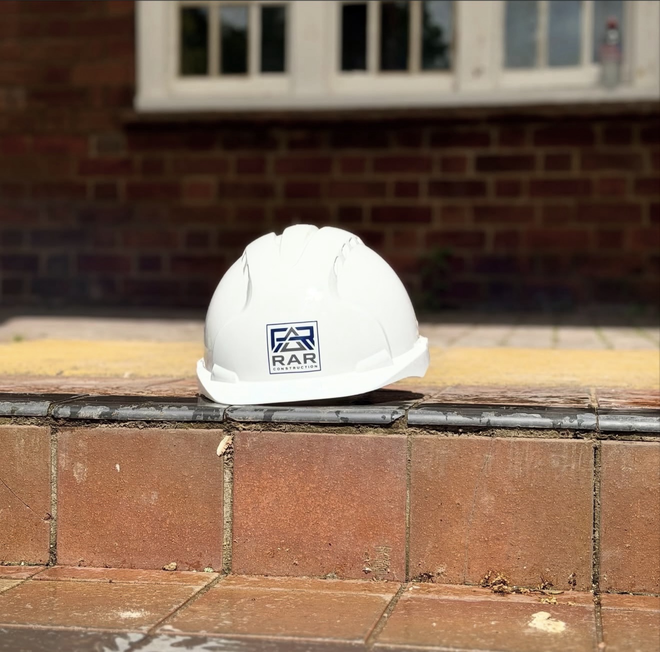 RAR Construction branded hard hat photographed on a brick wall.