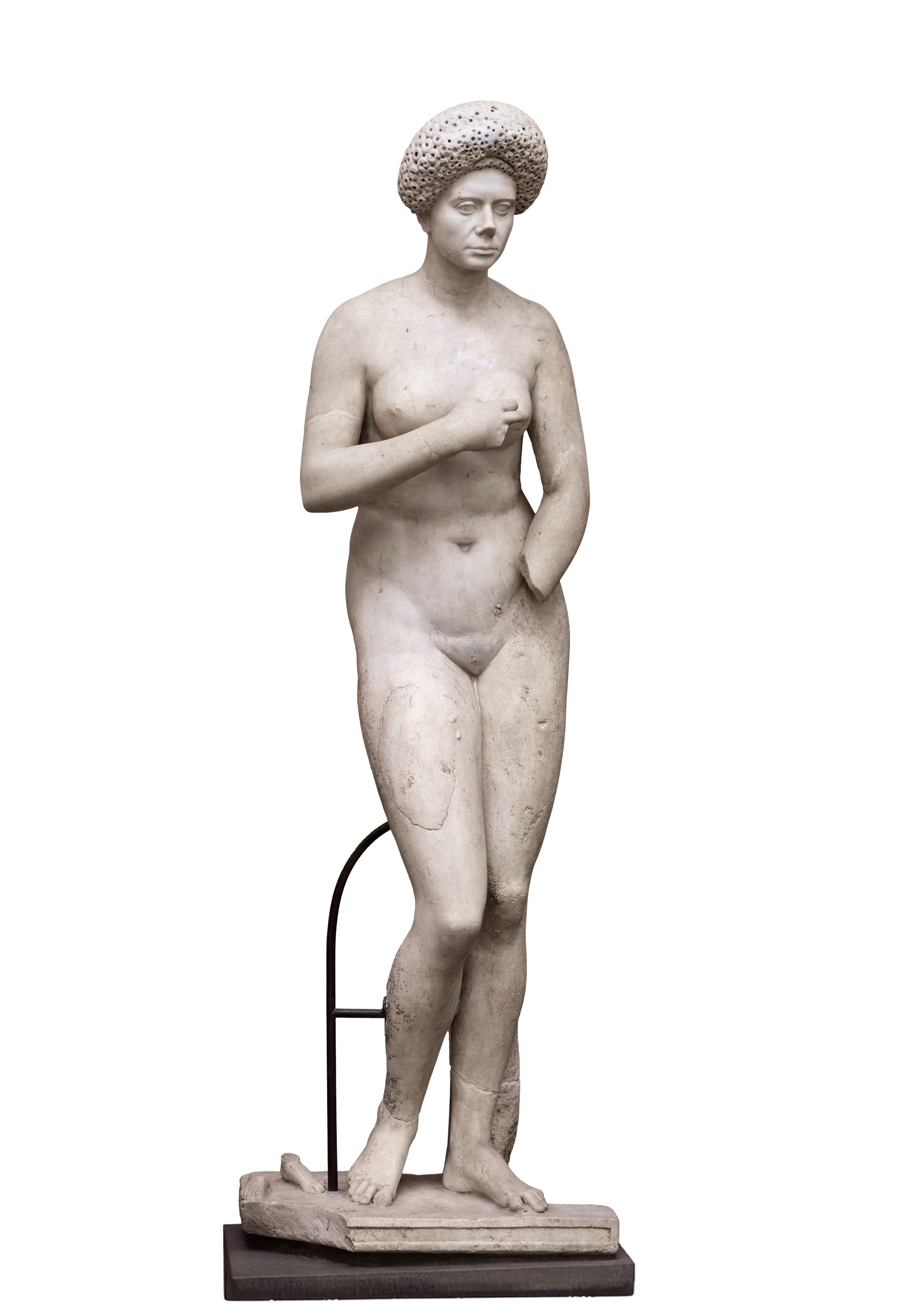 Skulptur af en nøgen kvinde med en stor, ruffled hat, stående på et rektangulært podium med en arm hævet og den anden ved siden.