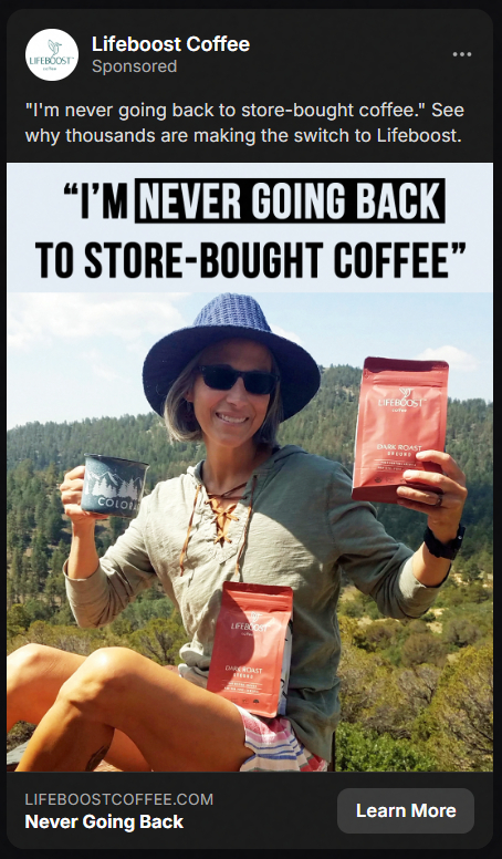Woman wearing sunglasses and a blue hat holds two bags of Lifeboost Coffee and a mug outdoors with a forested hill background, with text saying 'I'm never going back to store-bought coffee.'