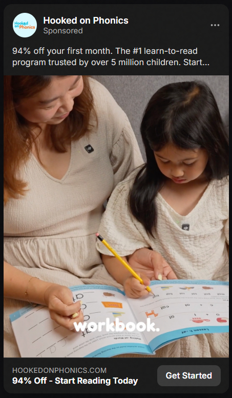 An adult woman and a young girl sitting together, both wearing beige tops, the girl holding a yellow pencil and working in a reading workbook while the woman guides her.