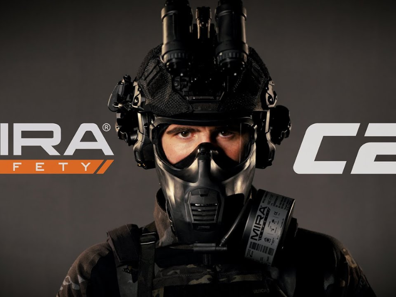 Person wearing tactical gear including a black helmet with mounted night vision goggles, a black gas mask labeled Mira Safety, and camouflage clothing against a dark background.