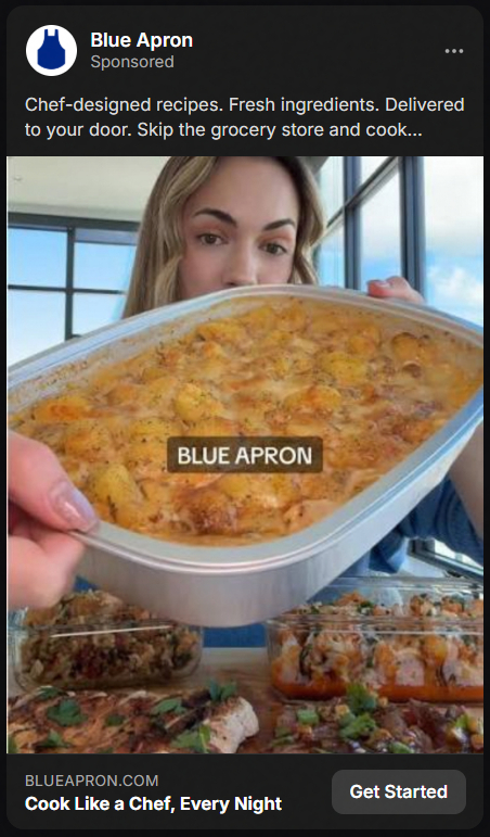 A woman holding a large tray of baked cheesy potato casserole labeled Blue Apron, with containers of various prepared meals in front of her on a table.