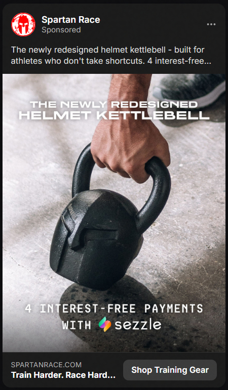 Close-up of a hand gripping a black kettlebell shaped like a Spartan helmet on a concrete floor, with text promoting a newly redesigned helmet kettlebell and four interest-free payments with Sezzle.