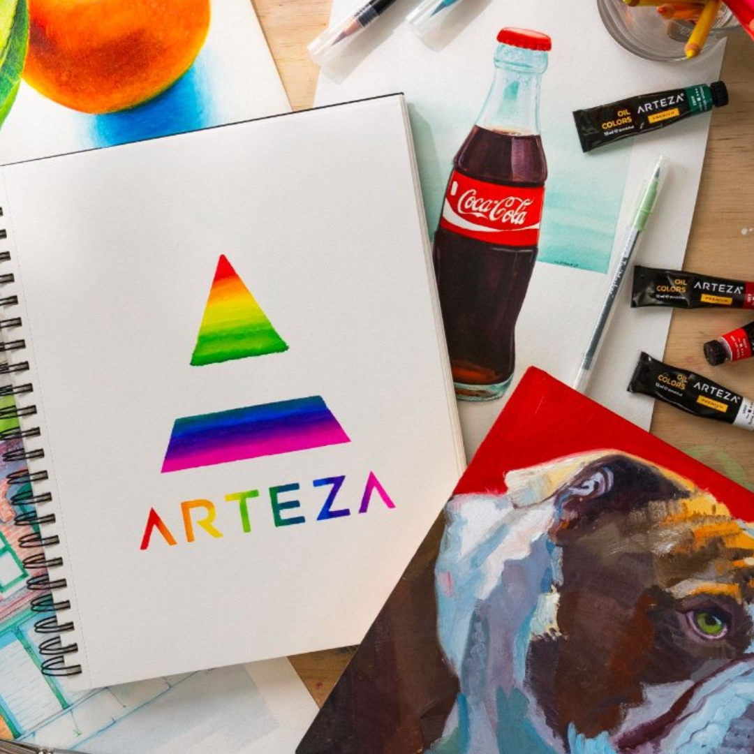 Art workspace with a spiral sketchbook displaying a rainbow-colored ARTEZA logo, tubes of Arteza oil colors, a Coca-Cola bottle, a green pen, colored pencils, and part of a painting of a dog with a red background.