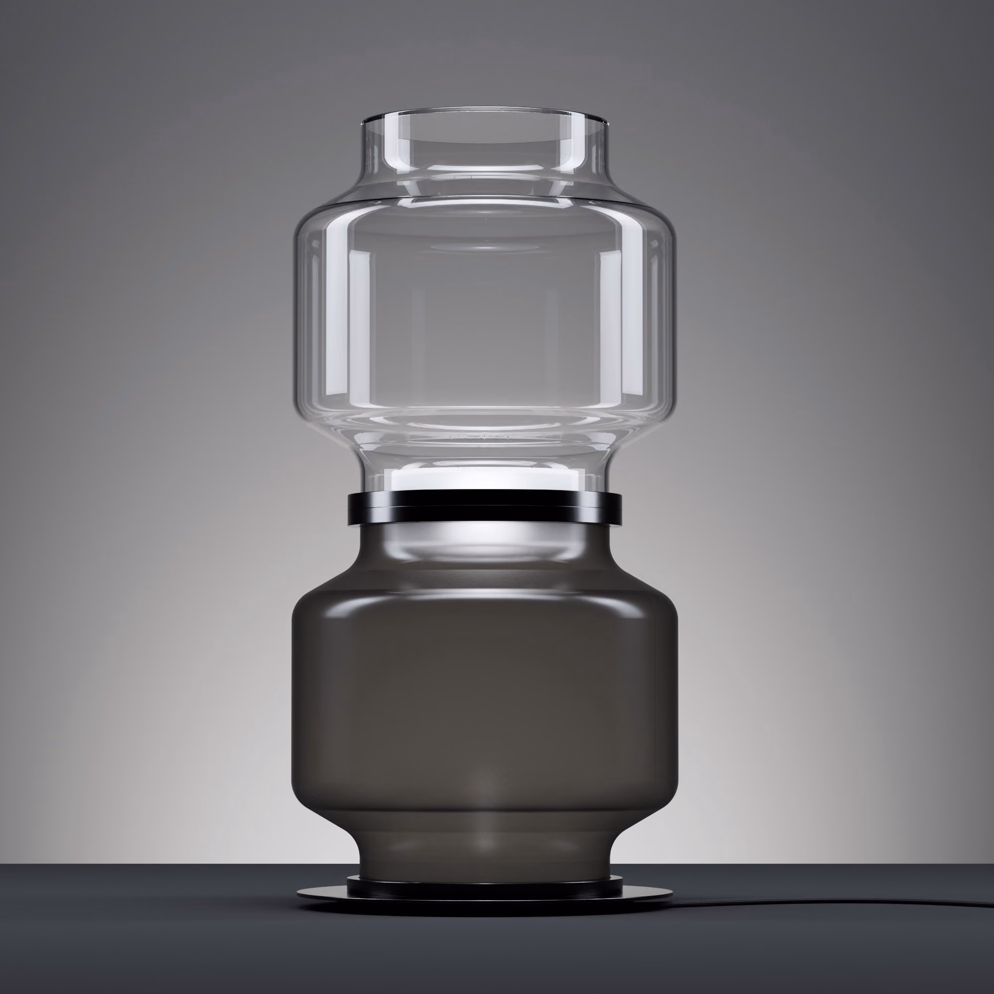 Modern table lamp with clear glass upper shade and smoky black lower base on a dark surface.