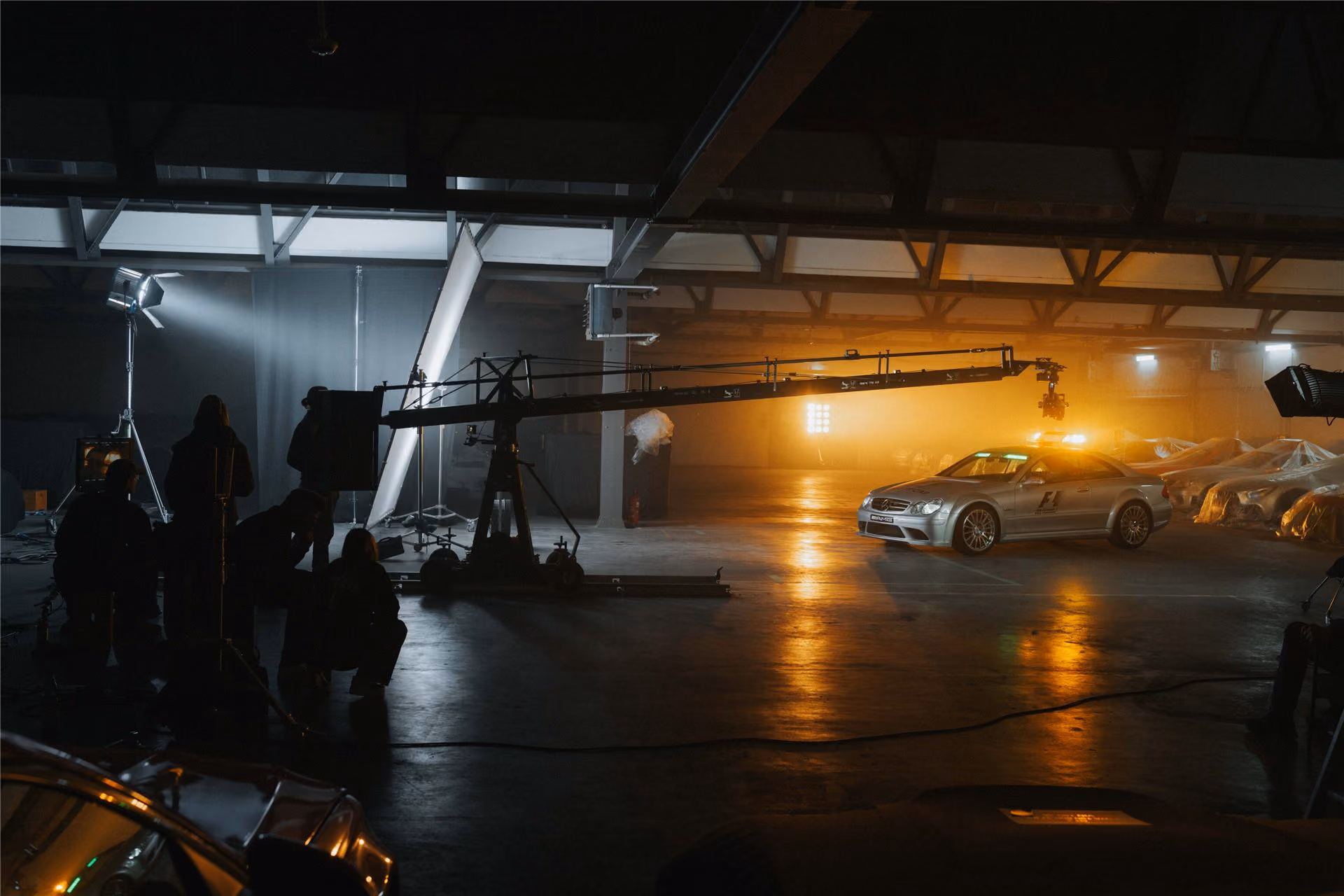 Film crew with a camera crane shooting a silver sports car in a dark hangar