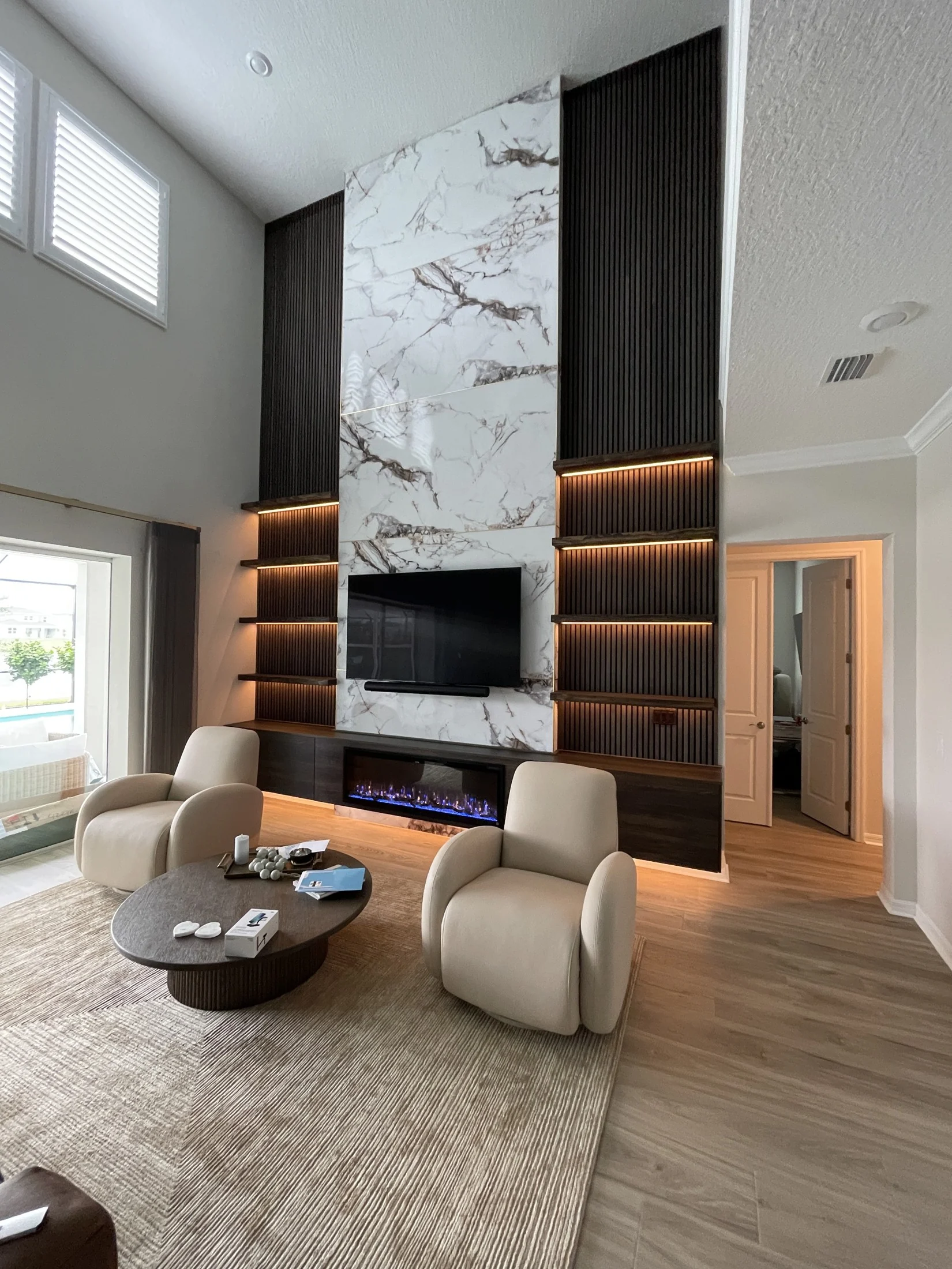 Completed two-story media wall with a marble-look center, dark slats, illuminated shelves and a fireplace