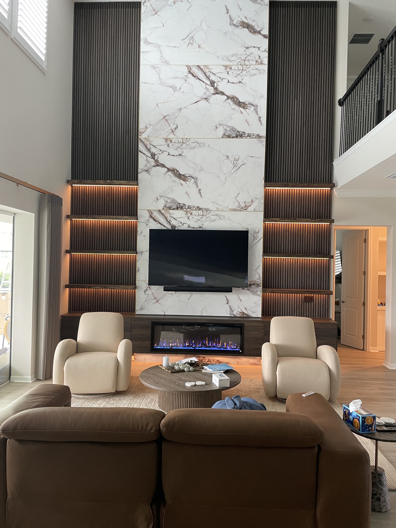 Finished media wall viewed from the seating area with warm shelf lighting and the fireplace on