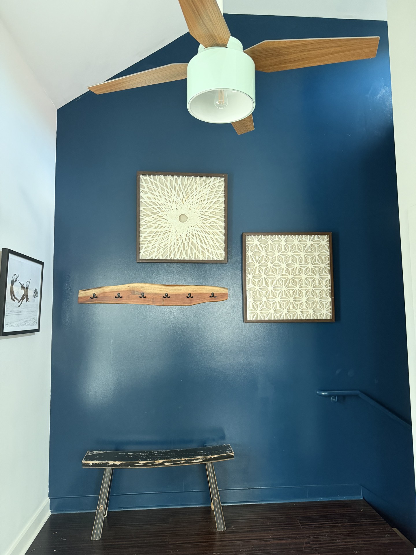 Office entryway with a deep blue wall, two framed cream textile artworks, a live-edge wooden coat rack, and a small wooden bench