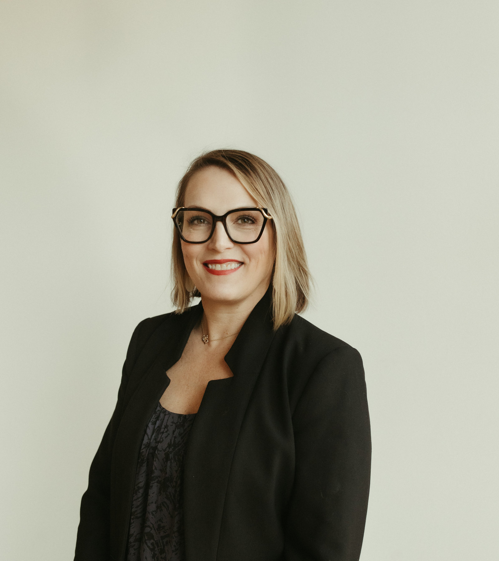 Kathleen Fugere, ARNP, smiling, wearing a black blazer and glasses, against a plain cream backdrop