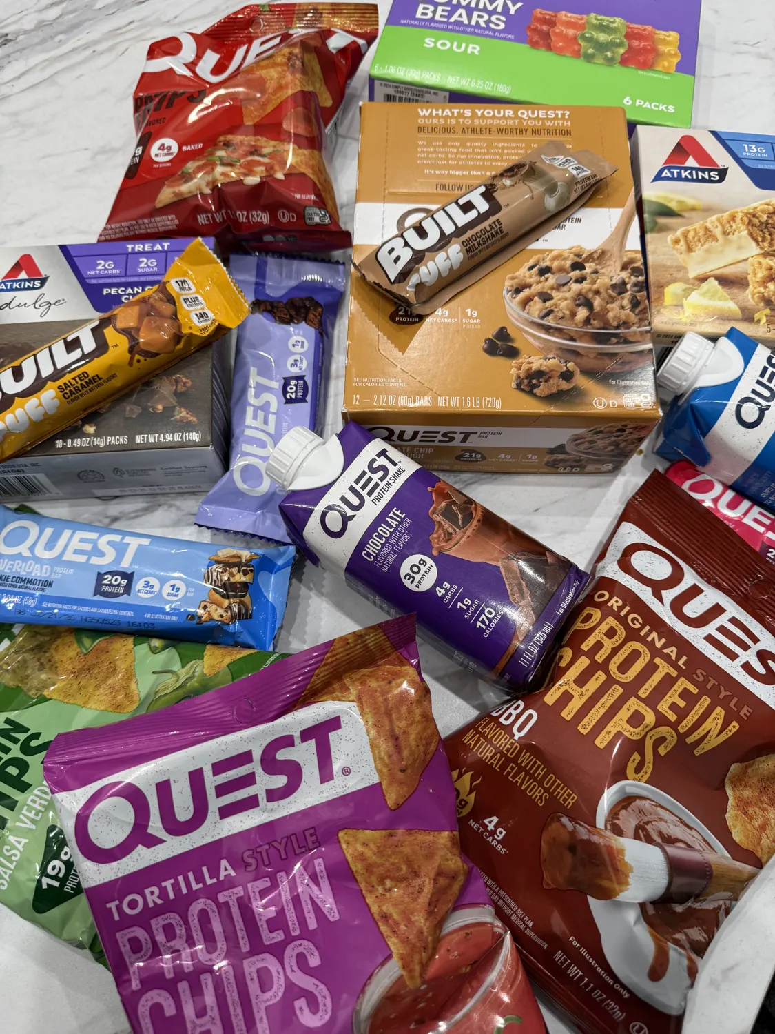 An assortment of nutrition snacks and beverages, including Quest, Atkins, and other brands