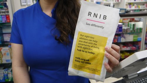 Pharmacy assistant holding an RNIB 'See differently' sight loss advice pharmacy bag