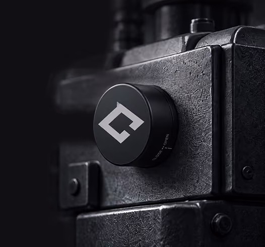 Close-up of a textured dark metal machine part with a round black knob featuring a white geometric logo in a dimly lit setting.
