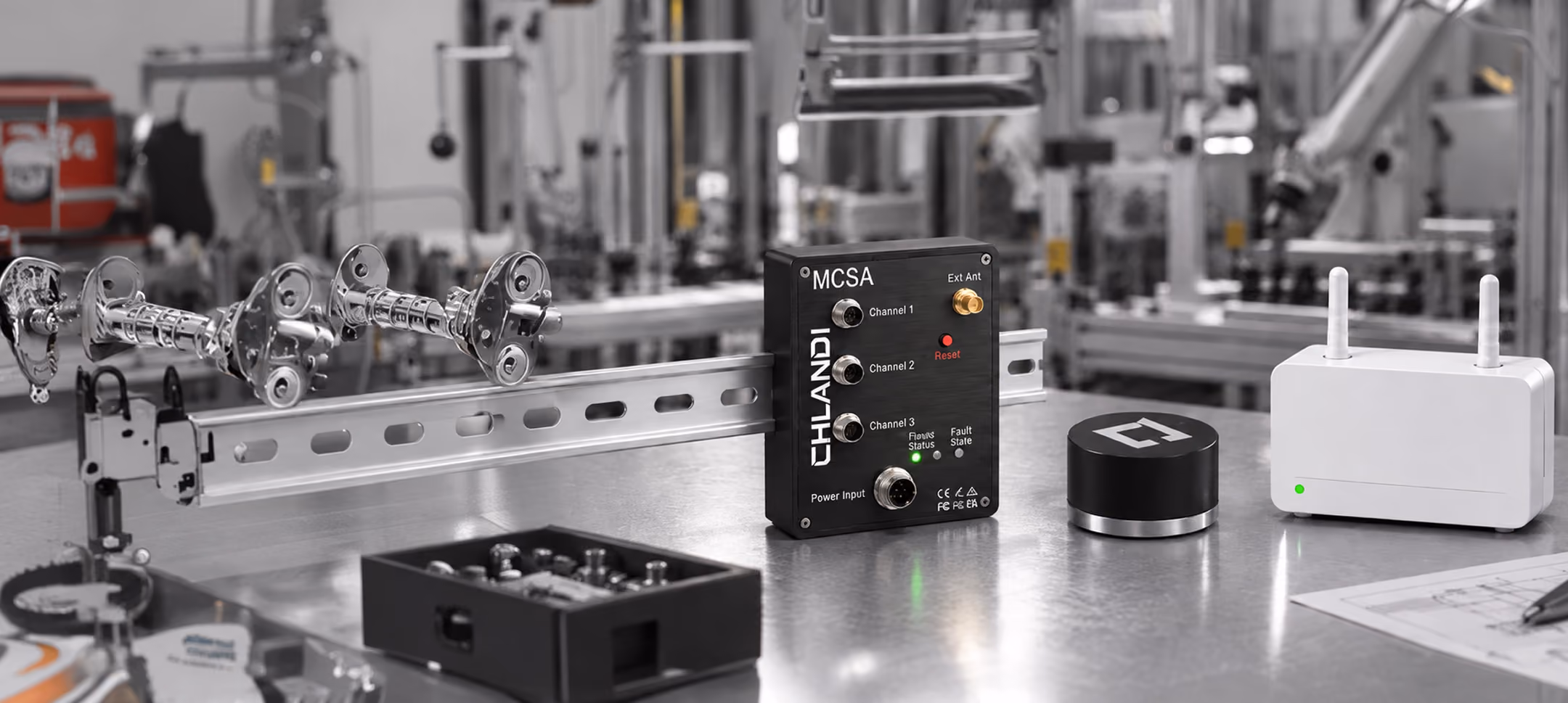 A metal surface in a factory or lab setting displaying three electronic devices: a black CHLANDI MCSA box with labeled channels and a reset button, a small black cylindrical device, and a white rectangular device with two antennas and a green indicator light. Background shows industrial equipment and piping.