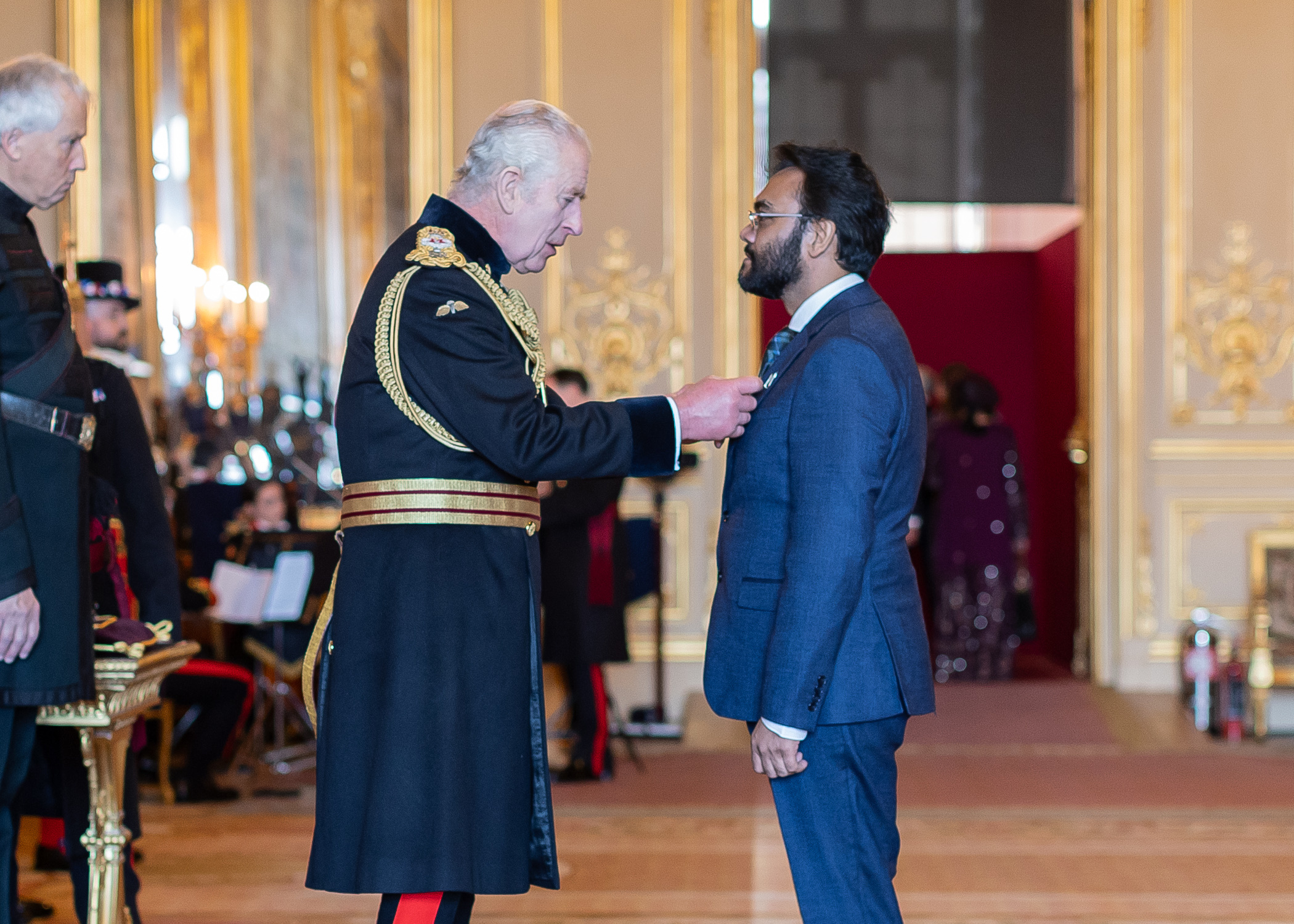 His Majesty King Charles III placing the MBE badge on Professor Naseem Naqvi’s chest