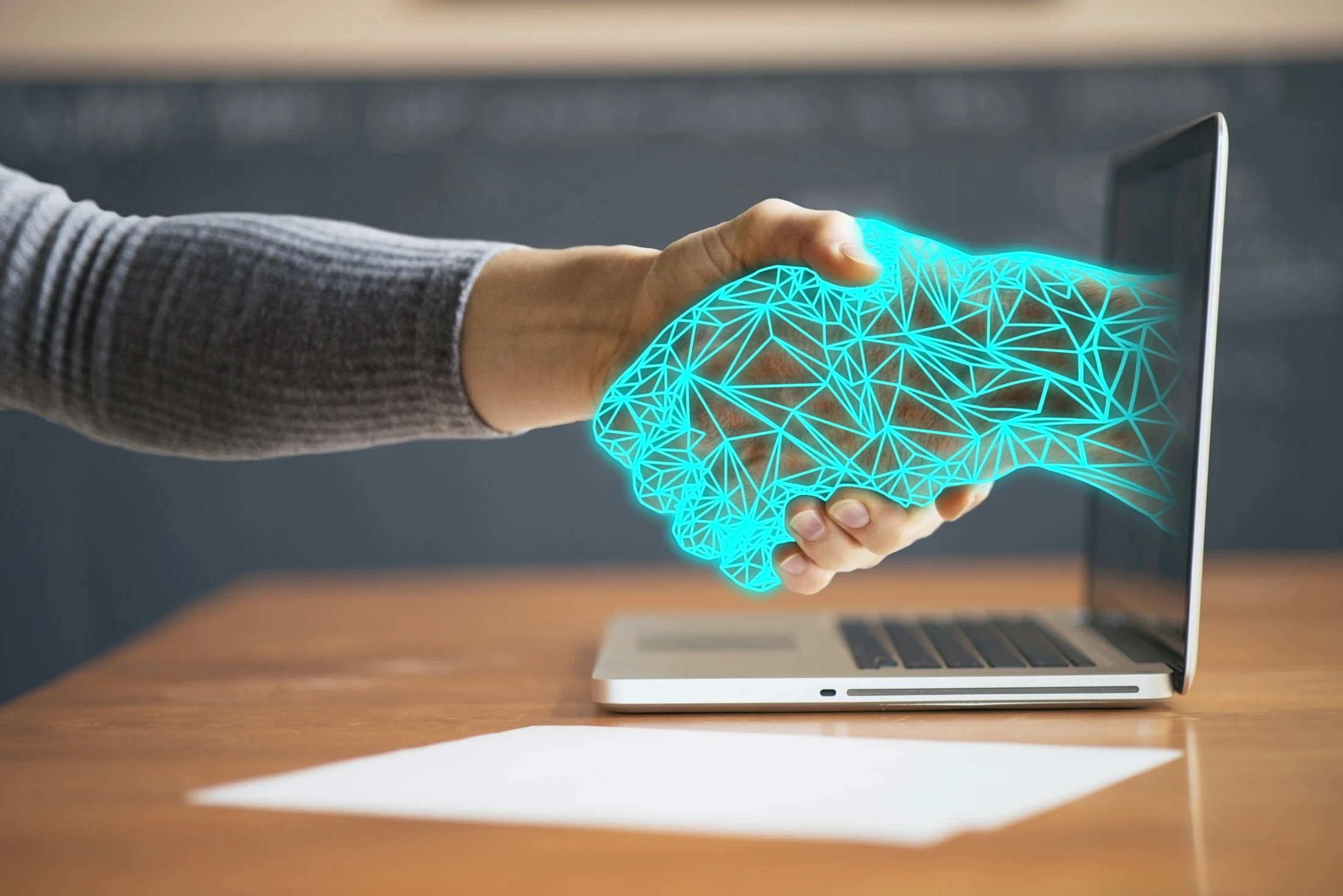 Human and digital hands meeting beside a laptop