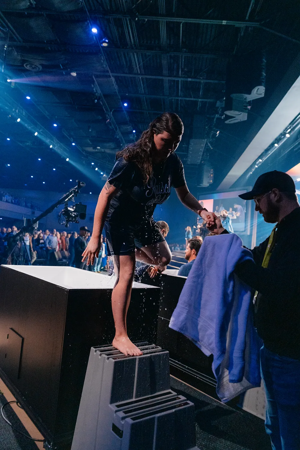 A young woman steps out of the baptism tank as a volunteer hands her a towel during a church service