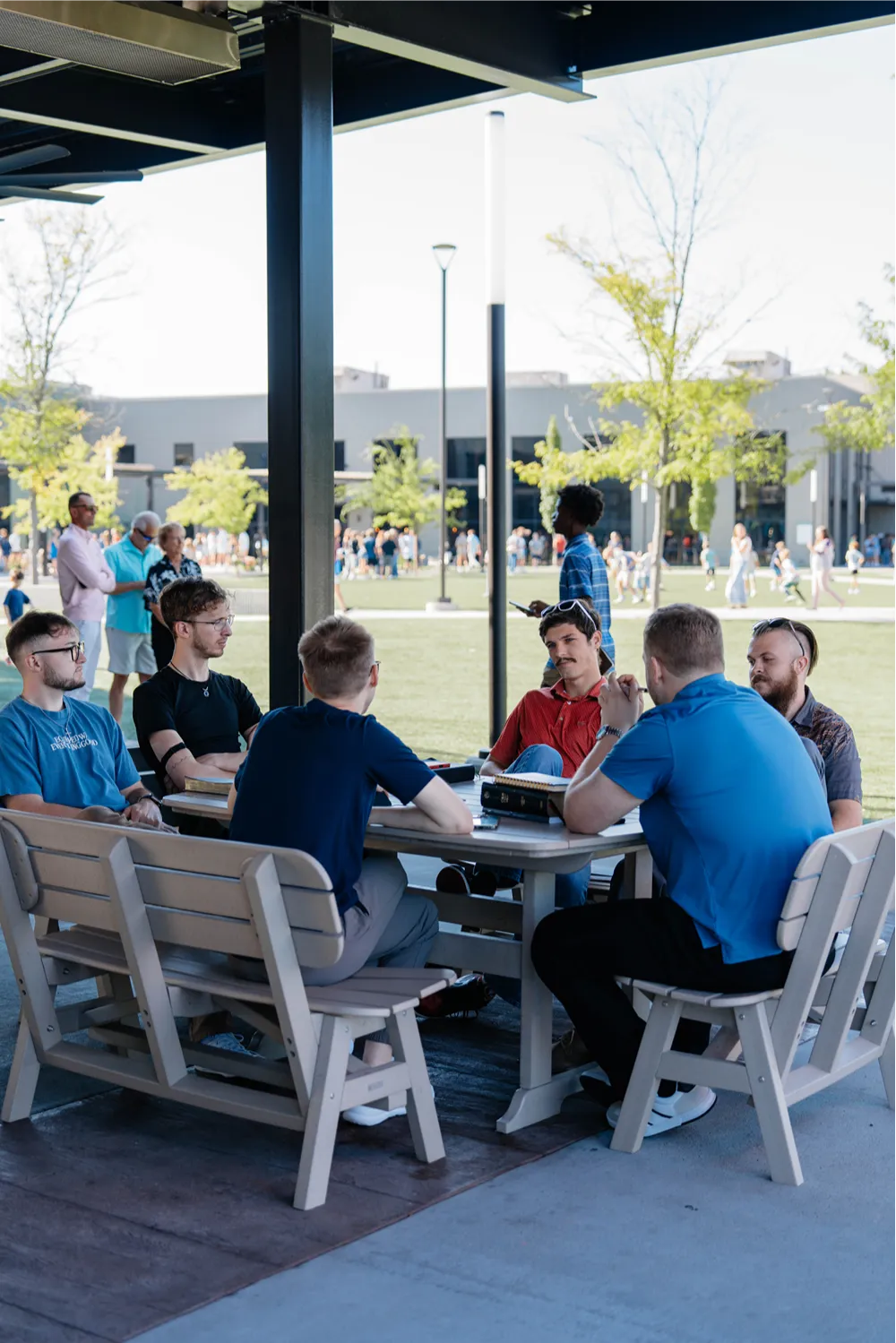 A group of men gather around an outdoor table with an open Bible on the church campus