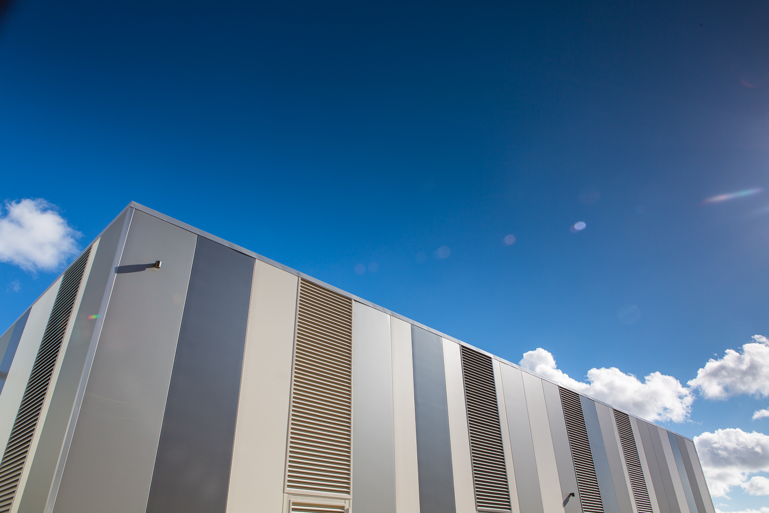 Commercial building with vertical grey and cream cladding panels and louvres against a blue sky