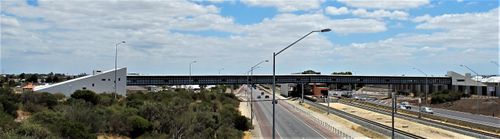 Wide view of a large metal-roofed building and elevated structure beside a major road