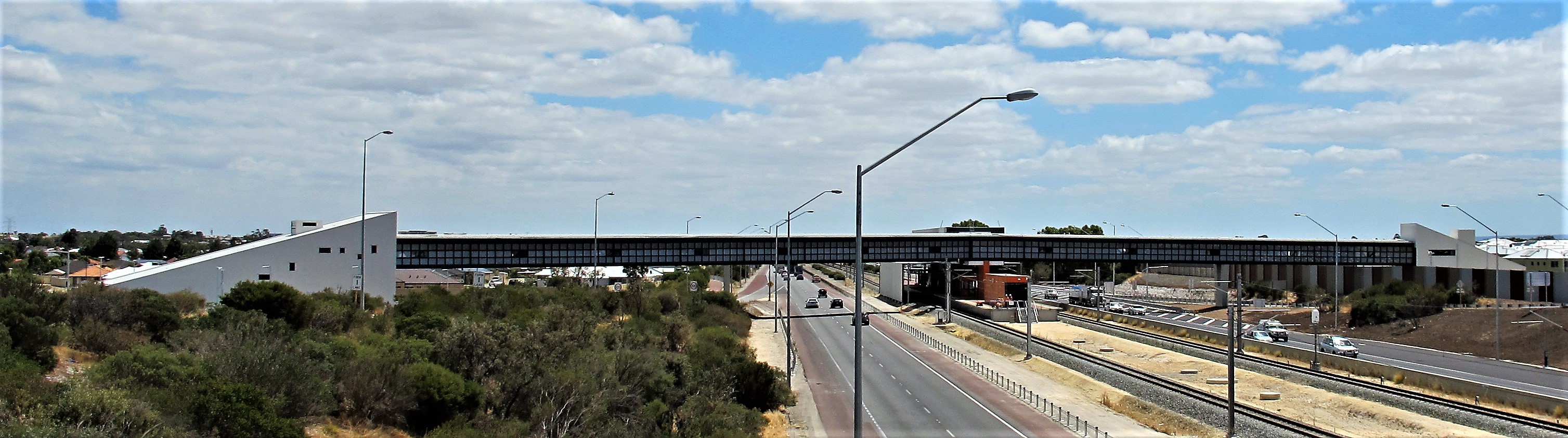 Wide view of a large metal-roofed building and elevated structure beside a major road