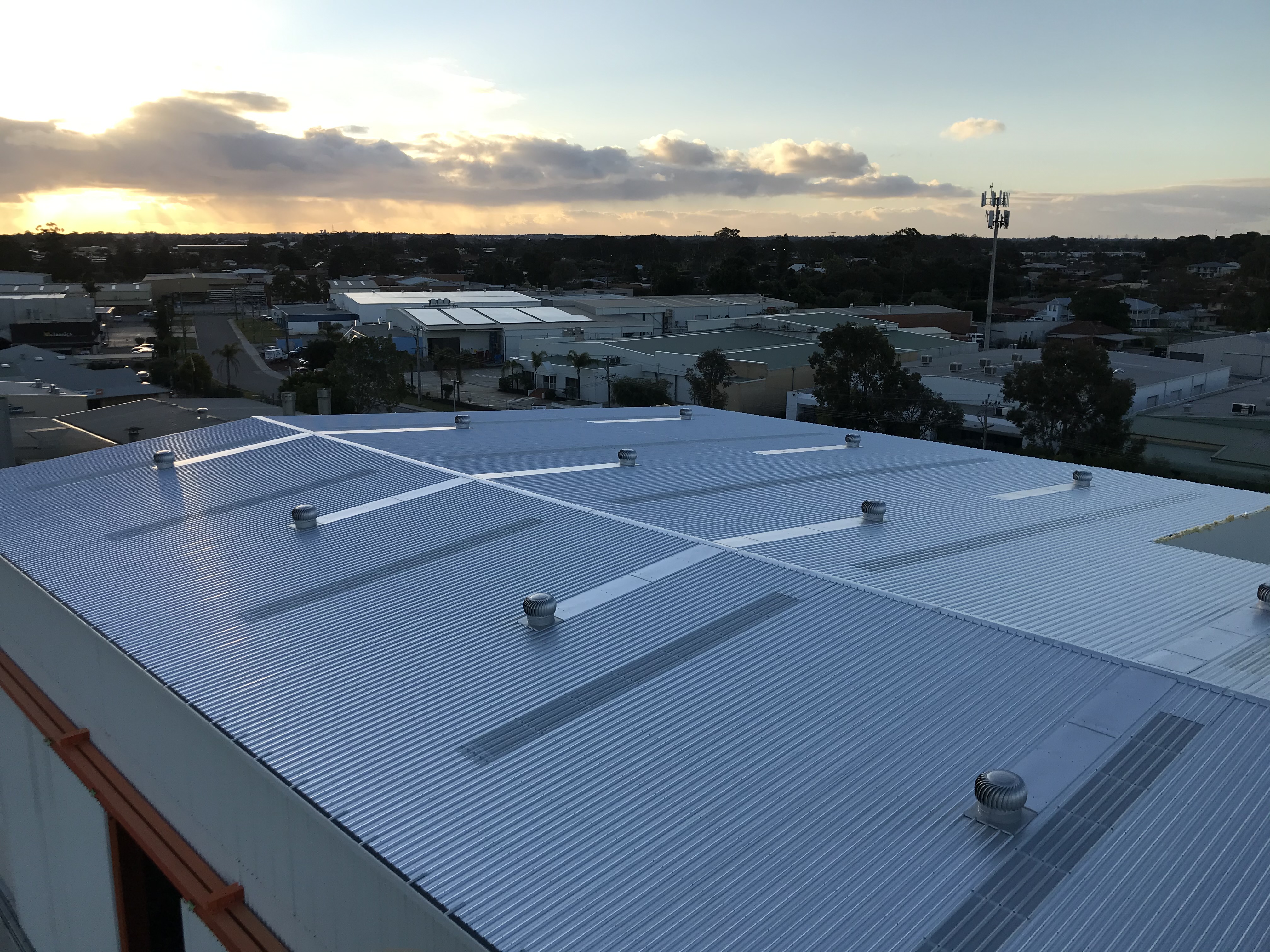 Commercial metal deck roof with skylights and roof vents over an industrial estate at dusk