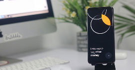 Smartphone on stand displaying a black screen with white and orange circular design and text about money.