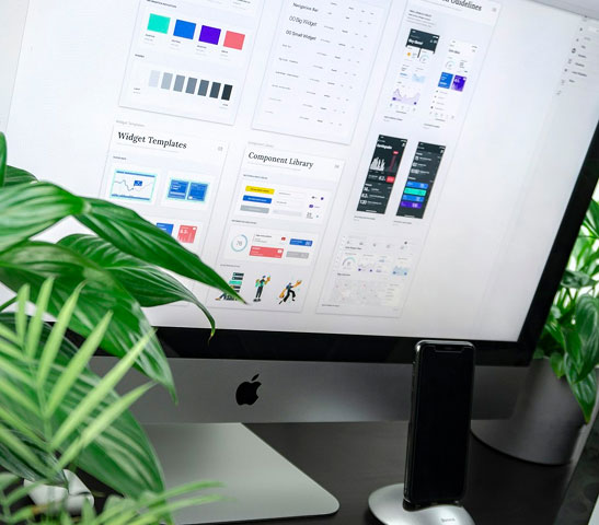 Apple iMac screen showing UI/UX design templates with plants and smartphone on desk.