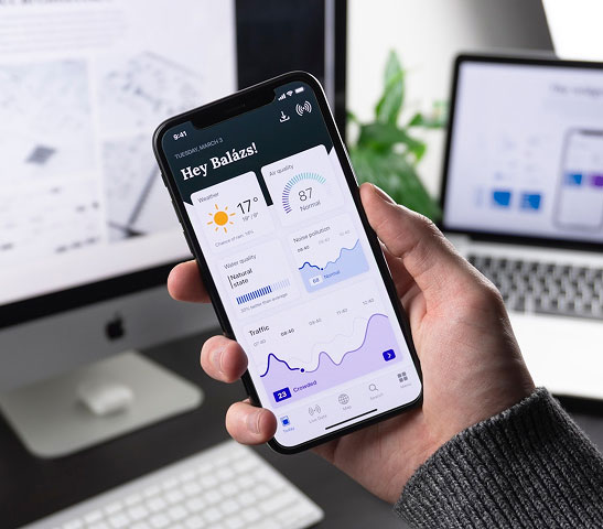 Hand holding a smartphone displaying a weather and noise pollution app dashboard.