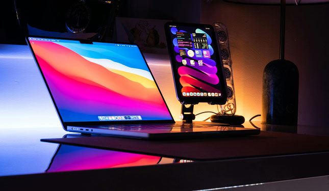 Open laptop with colorful screen beside a smartphone on a dark desk with blue backlight.