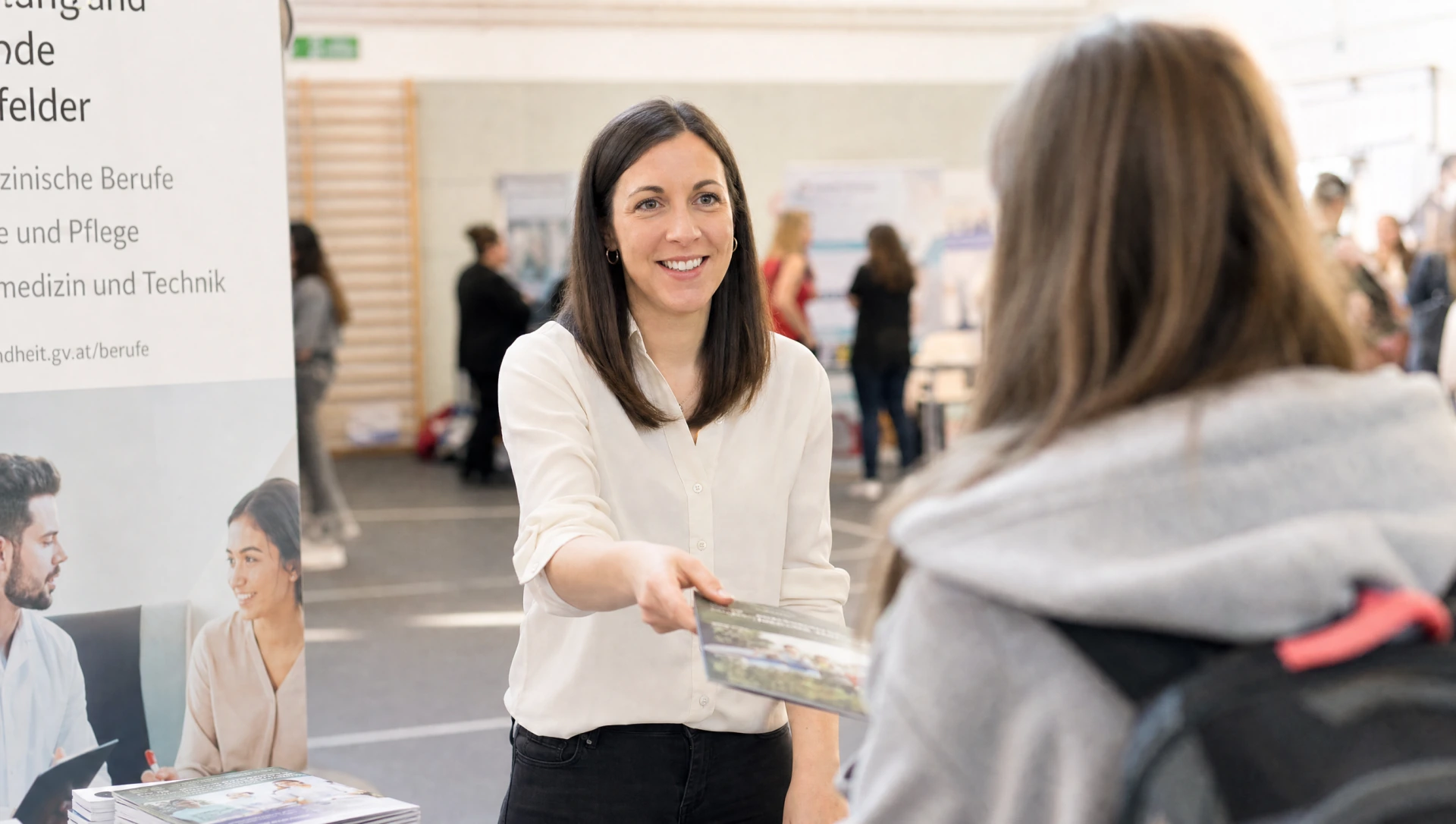 Frau am Berufsmessestand uebergibt laechelnd Informationsmaterial an Schuelerin mit Rucksack (KI-generiertes Bild)
